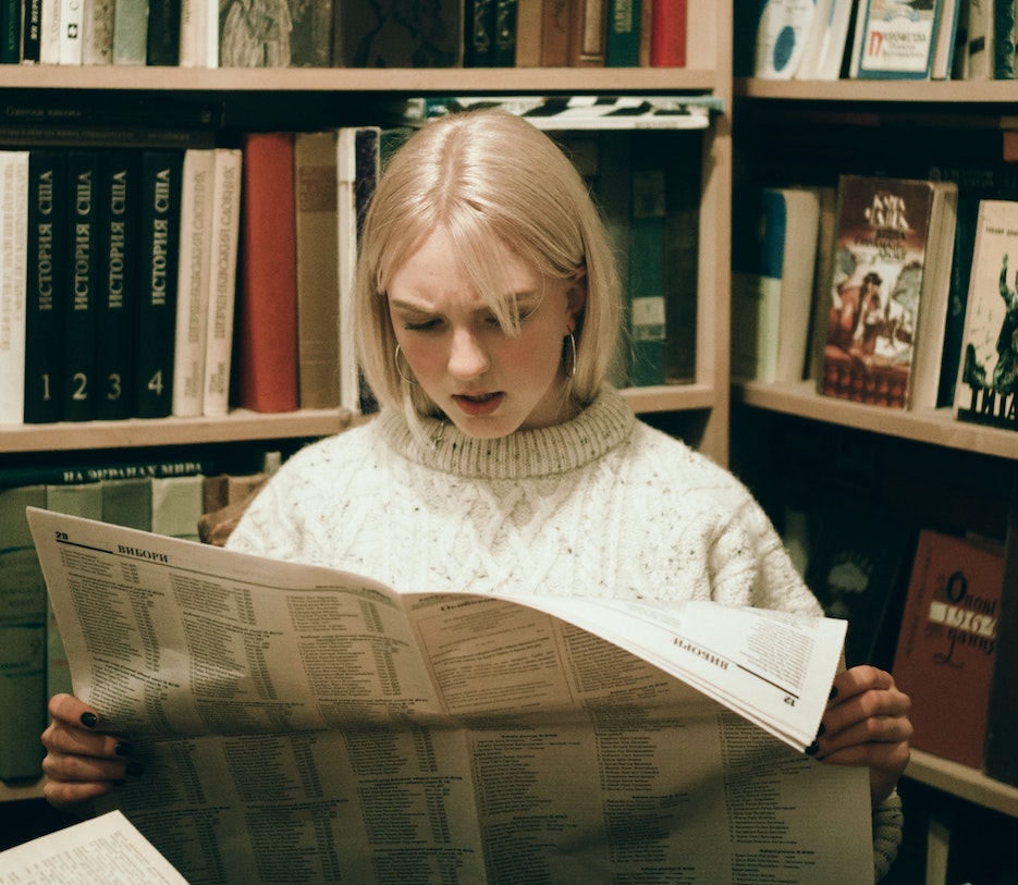 woman reading a newspaper with a dismayed expression, having just found out she was misquoted